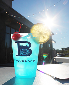 Close up of Brookland branded cup filled with blue cocktail sitting on a table.